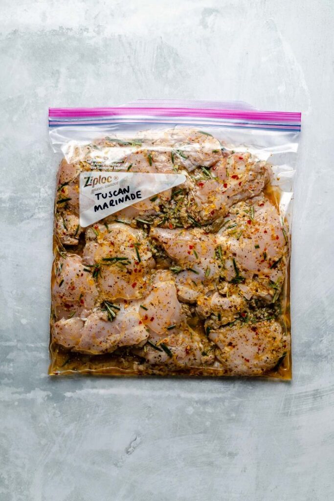 Raw chicken marinating in a Ziploc bag with Tuscan herbs and spices, ready for cooking.