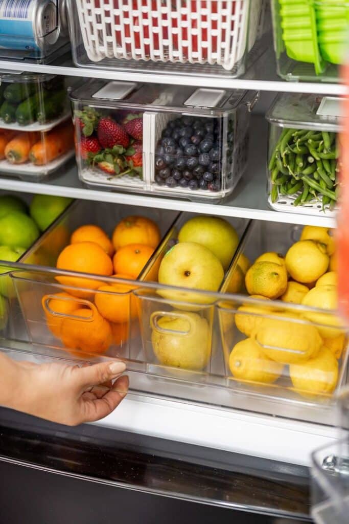 Organized fridge with fresh fruits and vegetables in clear containers for optimal storage and visibility.