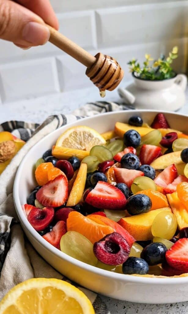 Fresh fruit salad with strawberries, blueberries, grapes, and more, drizzled with honey in a white bowl.