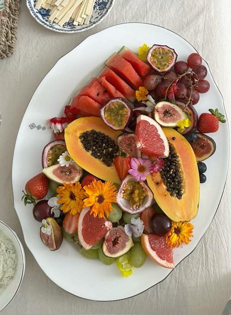 Vibrant fruit platter with papaya, grapes, figs, and passionfruit, garnished with edible flowers on a white plate.