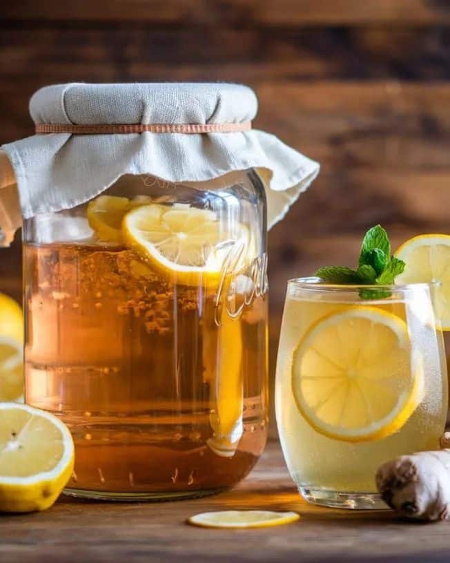 Jar and glass of lemon kombucha with ginger and mint on wooden table. Fermented drink in rustic setting.