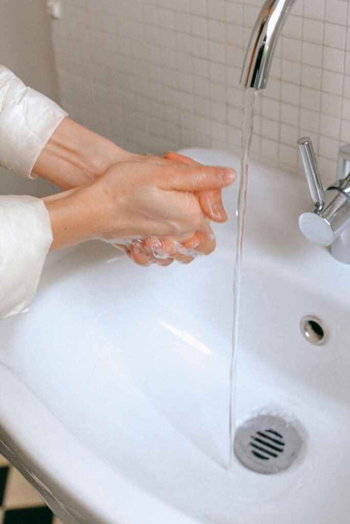 Hands washing with soap and water under a sink faucet for hygiene and cleanliness.