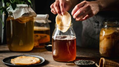 Hands preparing homemade kombucha with SCOBY in jars on a wooden table.