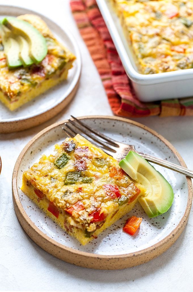 Vegetable frittata slice topped with avocado, served on a plate with a fork, showcasing a colorful breakfast dish.