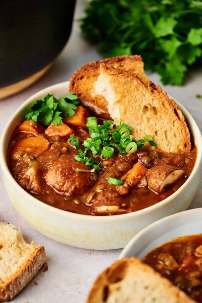 Hearty vegetable stew with crusty bread, garnished with fresh herbs, in a ceramic bowl. Perfect comfort food.