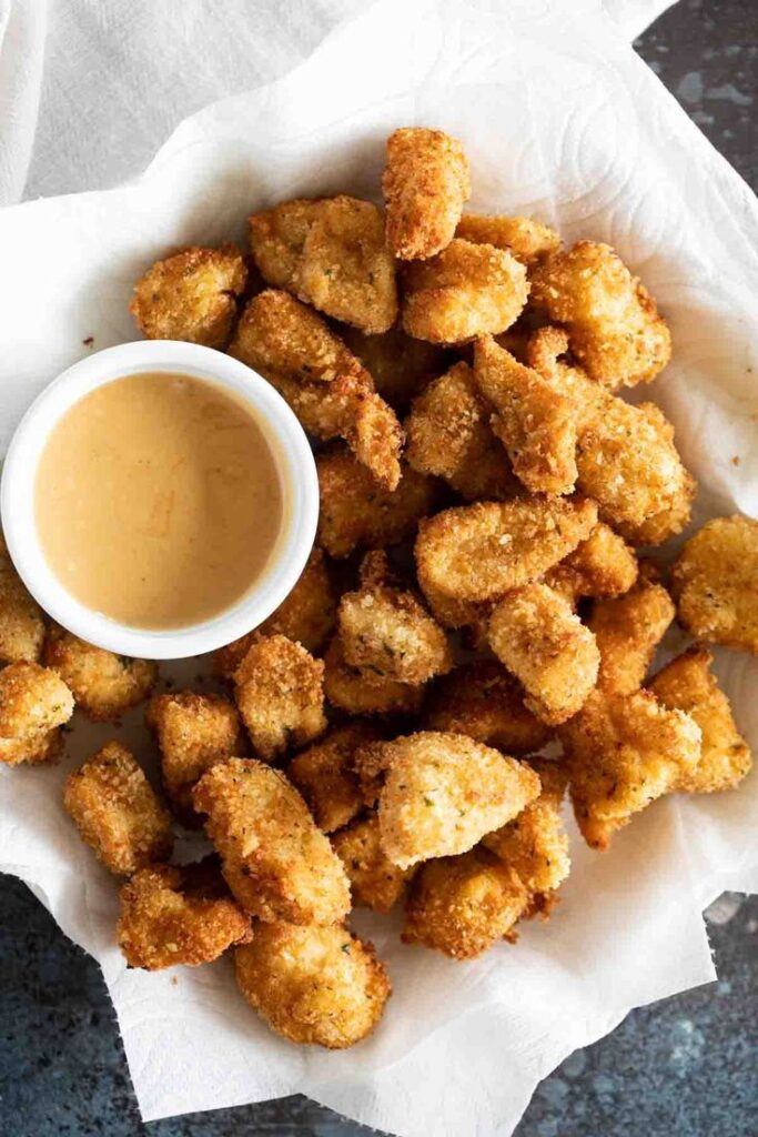 Crispy chicken nuggets served with a side of honey mustard sauce on a paper-lined tray.