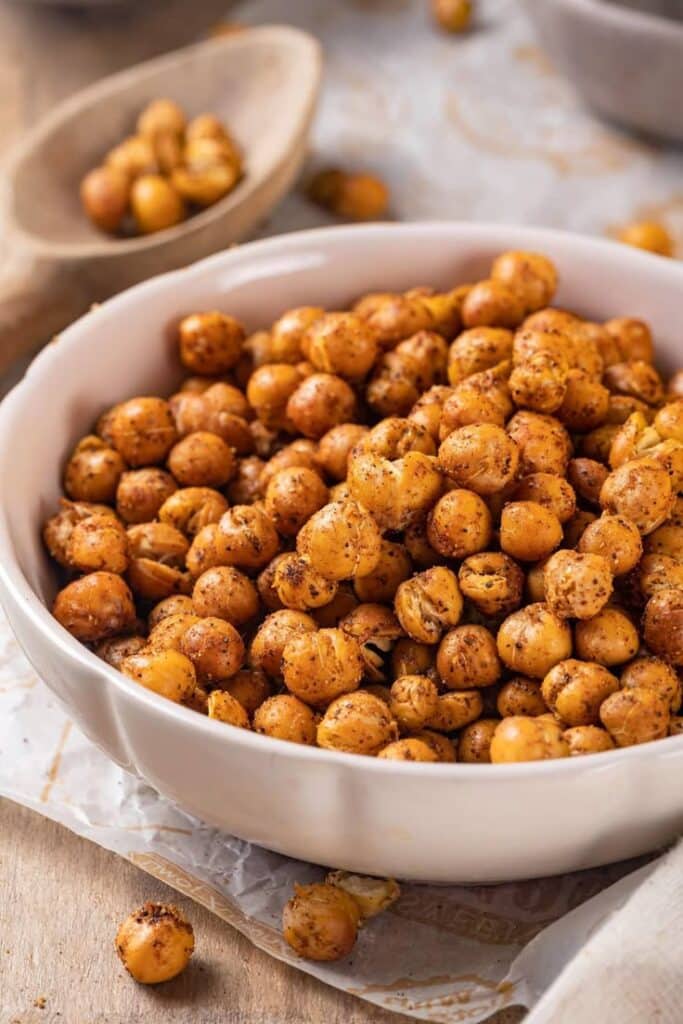 Bowl of spicy roasted chickpeas on a wooden table, healthy and crunchy snack option.