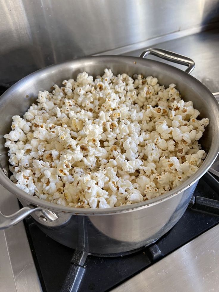Freshly popped popcorn in a large stainless steel pot on a kitchen stove.