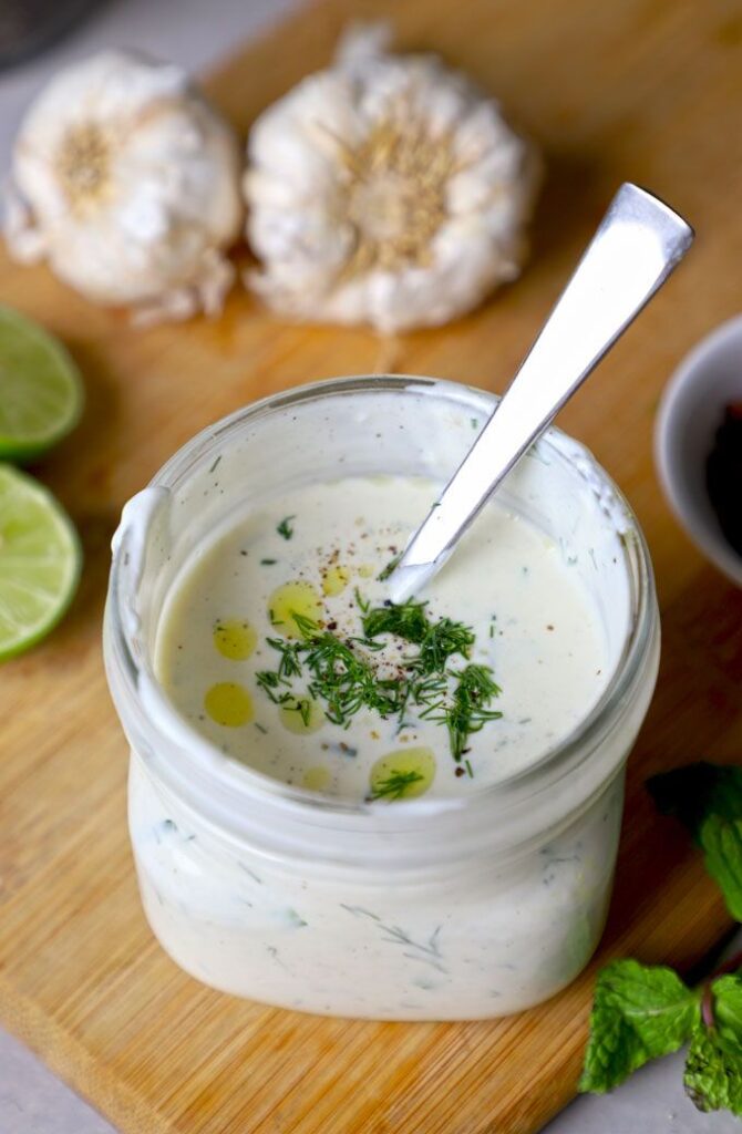 Glass jar of creamy ranch dressing with herbs, garlic, and lime on a wooden board.