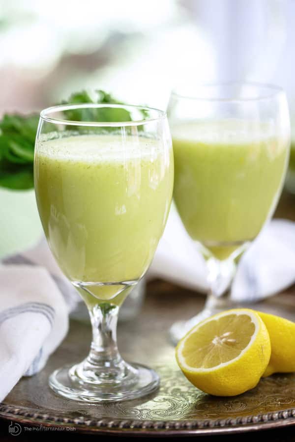 Two glasses of refreshing green smoothie with lemon and greens on a tray, perfect for a healthy beverage option.