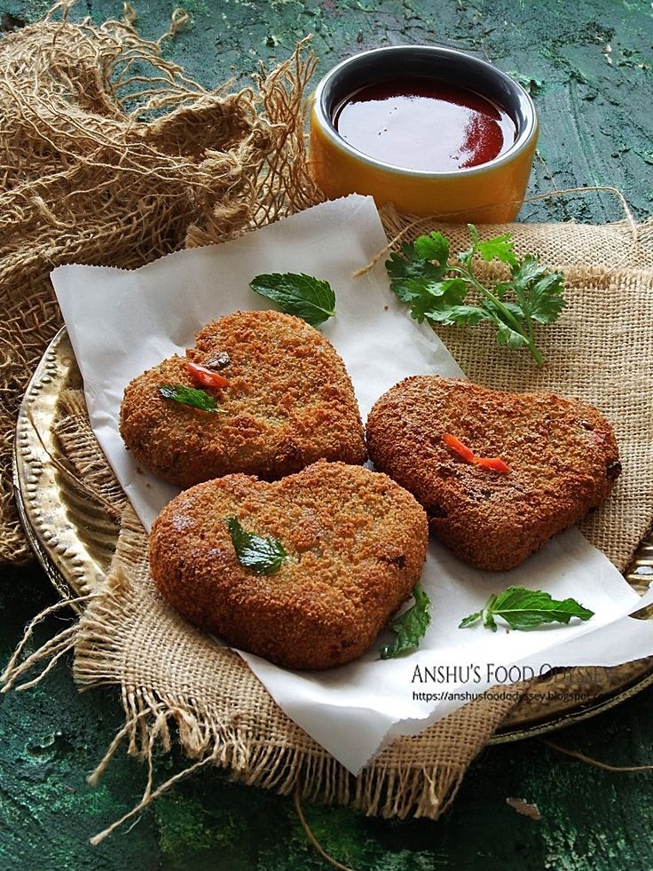Heart-shaped crispy cutlets garnished with herbs, served with a tangy sauce on rustic burlap.