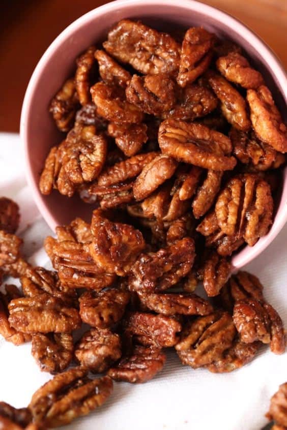 Sweet and spicy roasted pecans spilling from a pink bowl onto a white cloth.