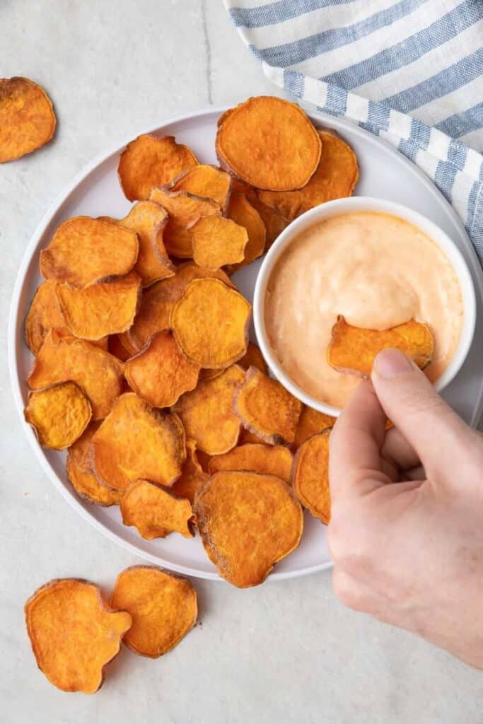 Homemade sweet potato chips with creamy dip on a white plate, perfect healthy snack option.