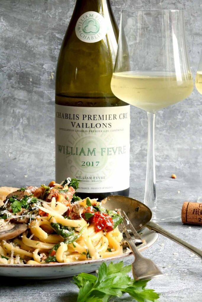 Bottle of Chablis wine with a glass and a plate of pasta garnished with fresh herbs and cheese.