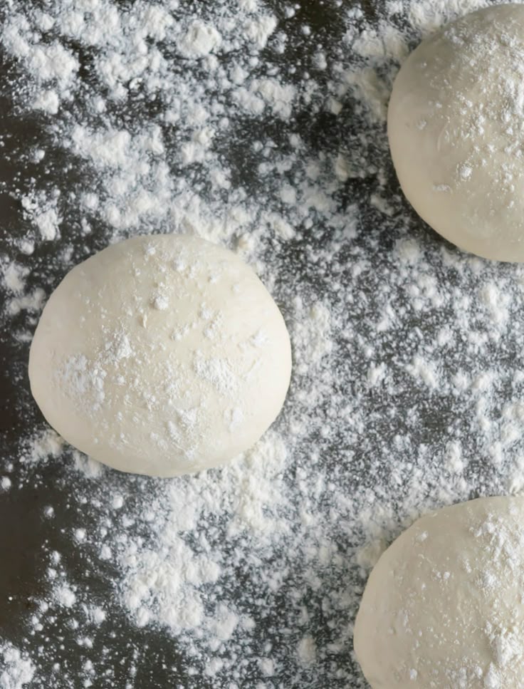 Flour-dusted dough balls on a surface, ready for baking or pizza making. Perfect for homemade bread recipes.