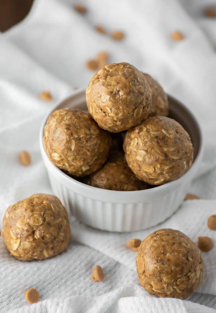 Homemade peanut butter oatmeal energy balls in a white bowl on a textured cloth surface.