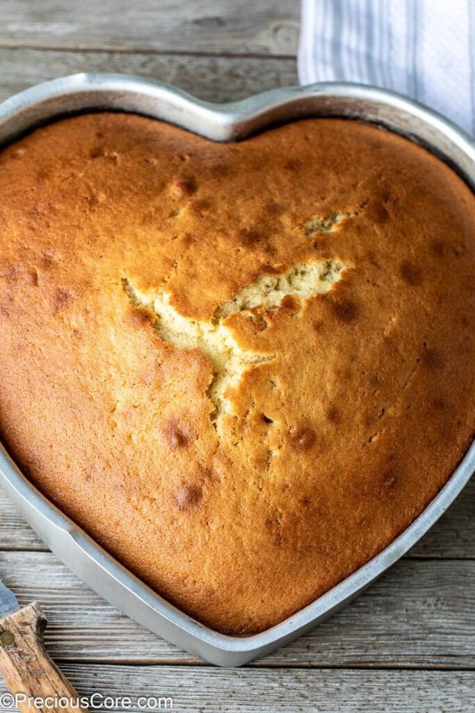 Heart-shaped golden cake in a metal pan on rustic wooden table. Perfect for special occasions or celebrations.