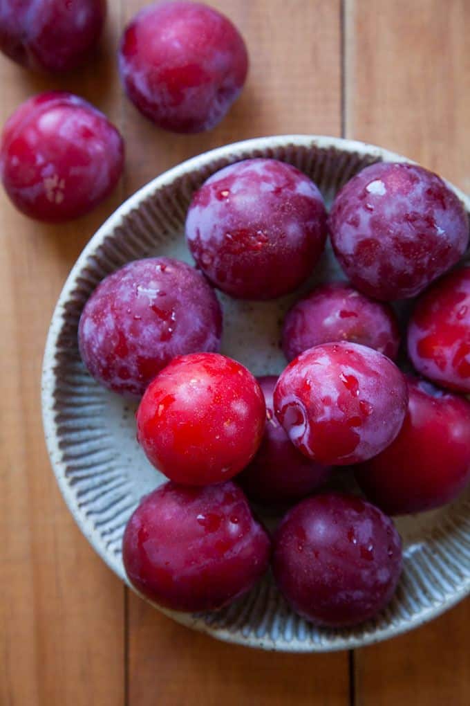 Fresh red plums in a ceramic bowl on a wooden table.