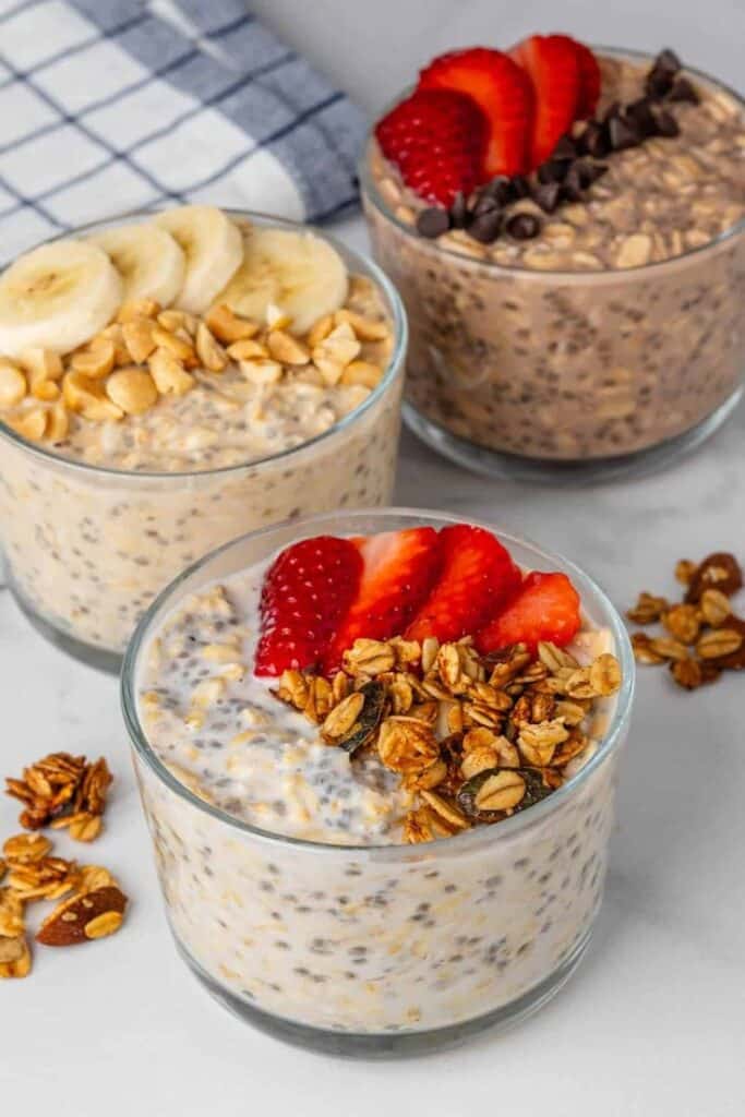 Three oatmeal bowls topped with strawberries, bananas, granola, and peanuts on a table.