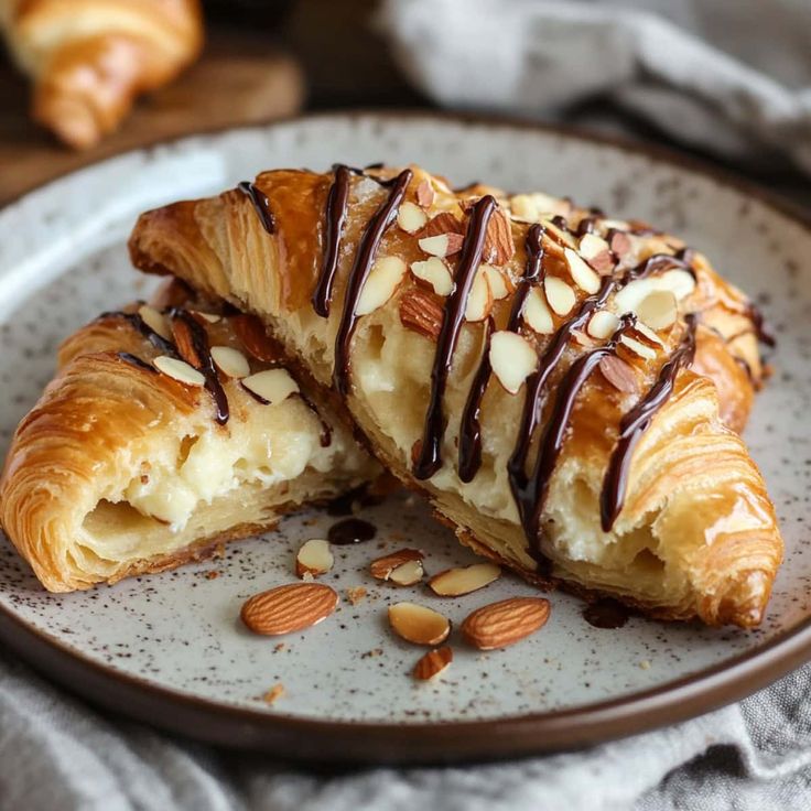 Almond chocolate croissant on a plate, filled with creamy custard and topped with sliced almonds and chocolate drizzle.