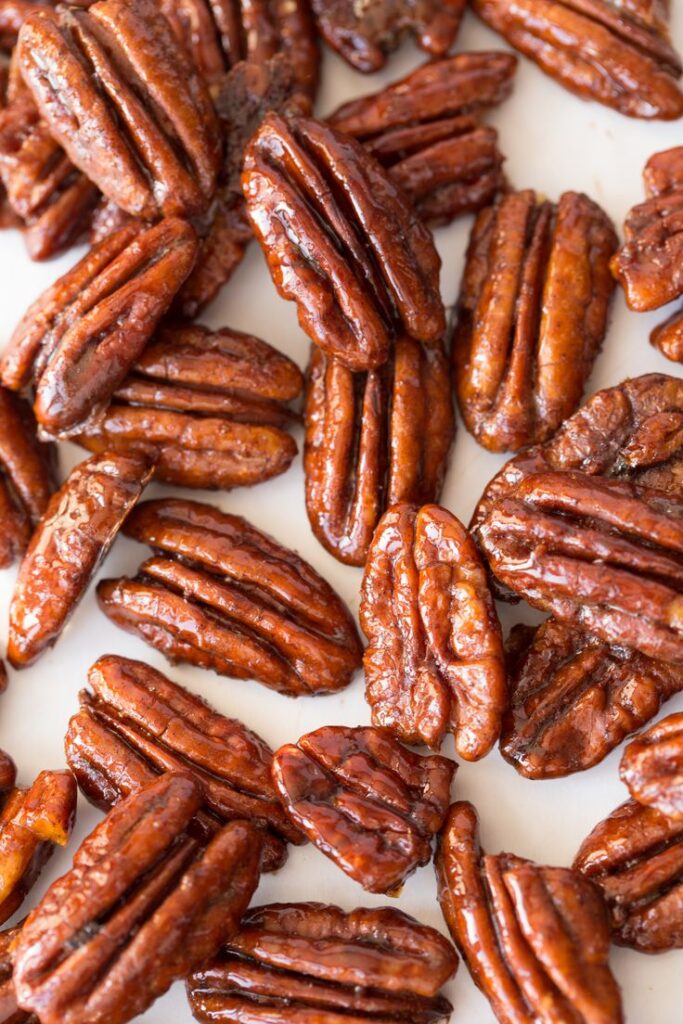 Close-up of glazed pecans on a white surface, showcasing their rich, glossy texture. Perfect for snacking or recipes.