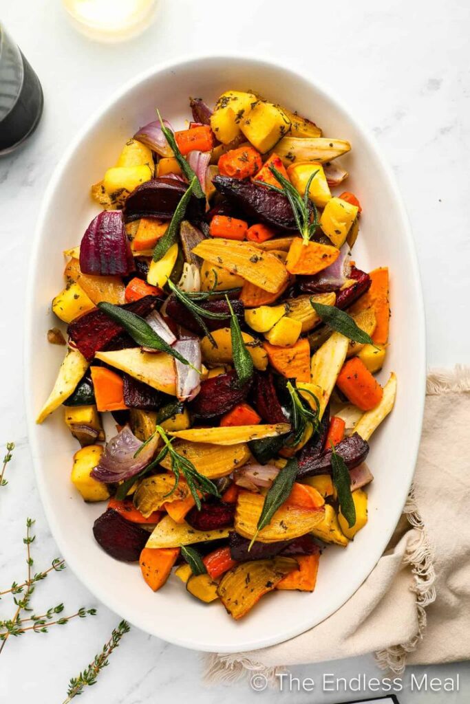Delicious roasted vegetables with herbs, featuring carrots, beets, and potatoes in a white serving dish.