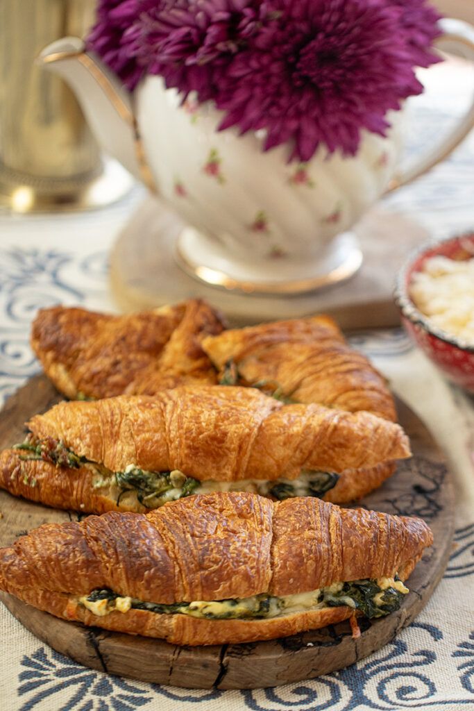 Fresh croissants with spinach filling on a wooden platter, accompanied by a floral teapot in the background.
