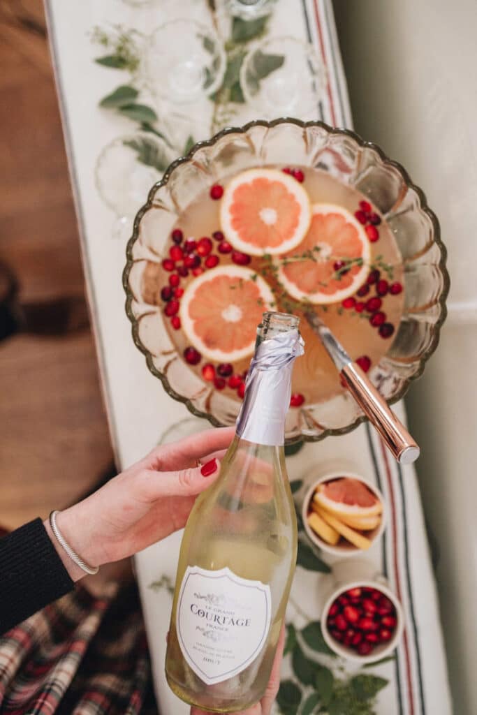 Festive punch bowl with grapefruit slices, pomegranate seeds, and sparkling wine held above for pouring.
