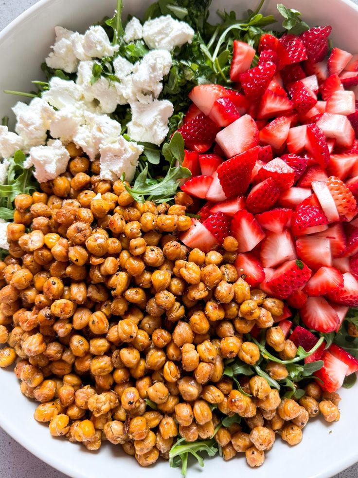 Fresh salad with spicy roasted chickpeas, chopped strawberries, and creamy cheese on a bed of greens.