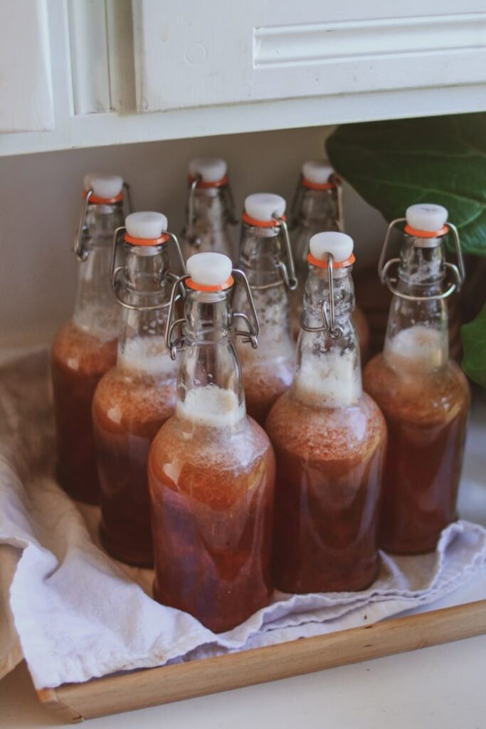 Glass bottles of homemade kombucha with flip-top caps on a wooden tray, ready for fermentation.