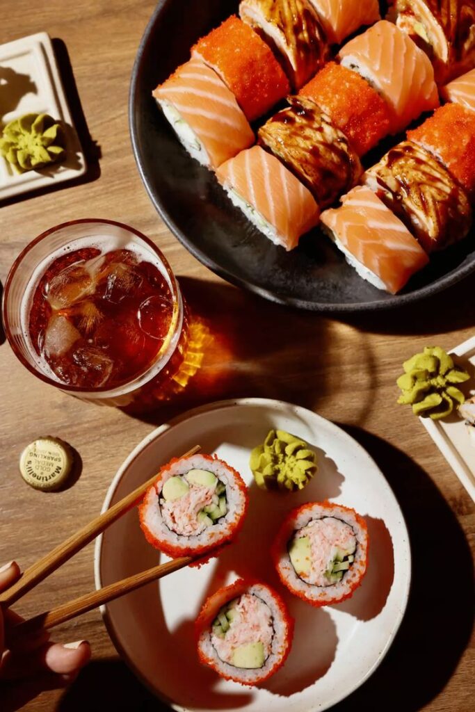 Assorted sushi rolls with salmon and crab served with iced drink on a wooden table, garnished with wasabi.