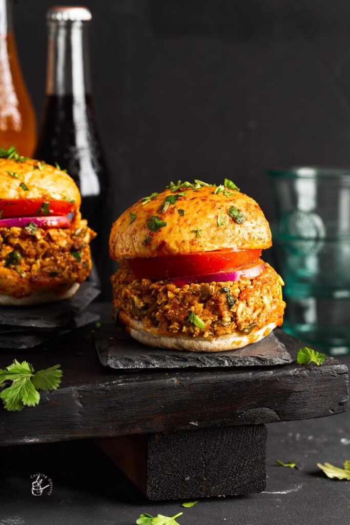 Delicious spicy burger with vegetables, garnished with herbs, served on a dark slate board. Perfect for a gourmet meal.