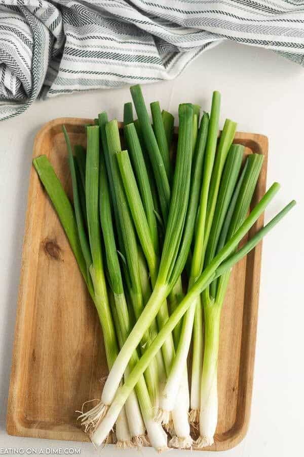 Fresh green onions on a wooden tray, perfect for adding flavor to salads and dishes.