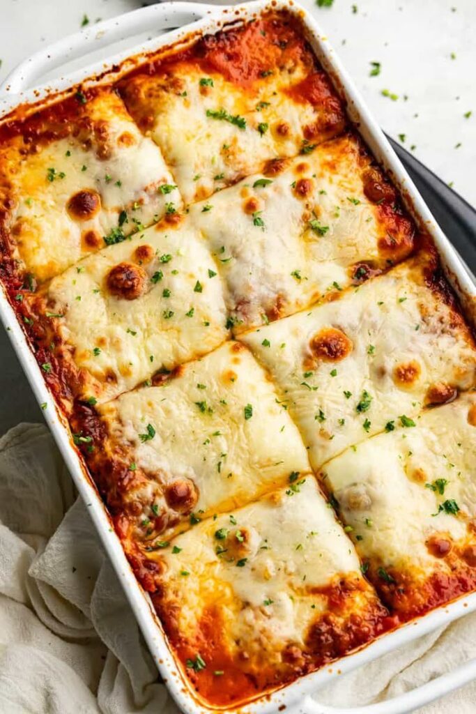 Delicious homemade lasagna with golden cheese topping in a white baking dish, sprinkled with fresh parsley.