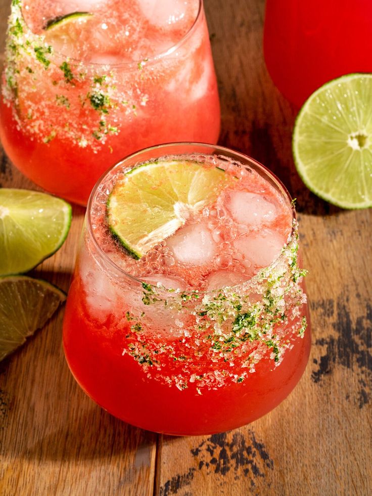 Refreshing strawberry cocktail with ice and lime slices, garnished with a salted rim on a wooden table.