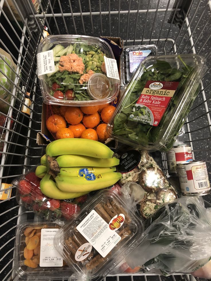 Shopping cart filled with fresh produce and groceries, including bananas, spinach, mandarins, and more.
