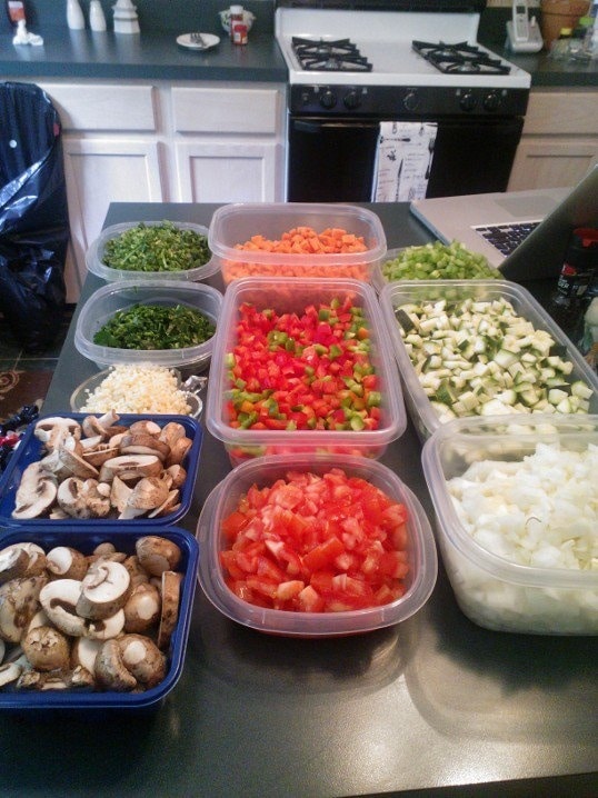 Chopped vegetables in containers on kitchen counter, including mushrooms, peppers, onions, and tomatoes for meal prep.