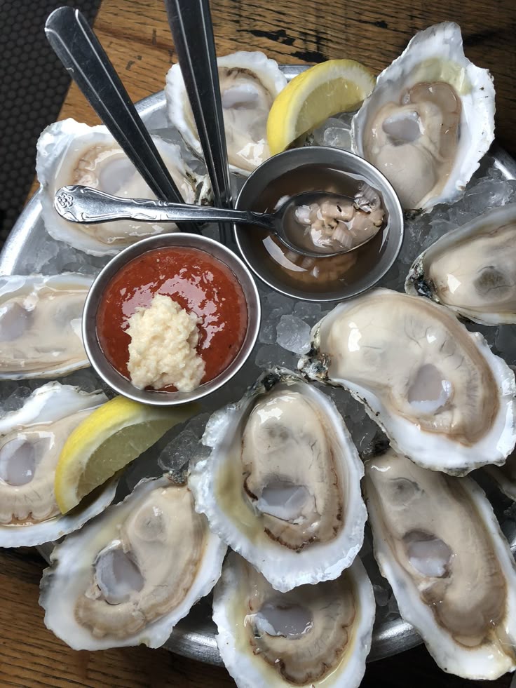 Plate of fresh oysters on ice with lemon wedges and cocktail sauce.