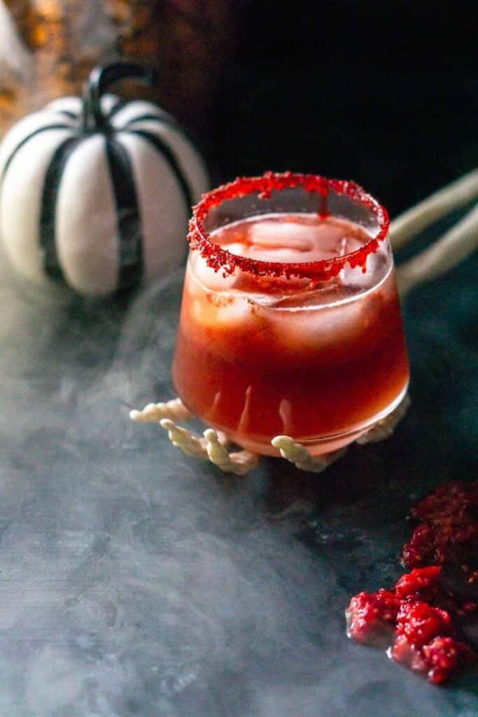 Spooky Halloween cocktail with red rim, smoky effect, and pumpkin decor on a dark table.
