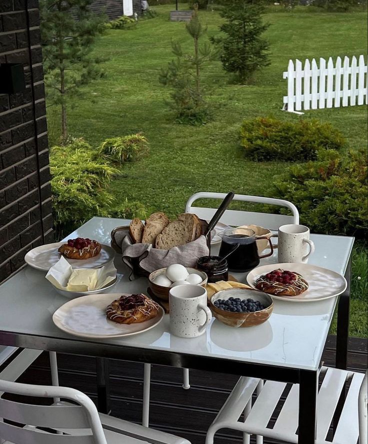 Outdoor table with breakfast pastries, bread, eggs, and coffee in a garden setting.