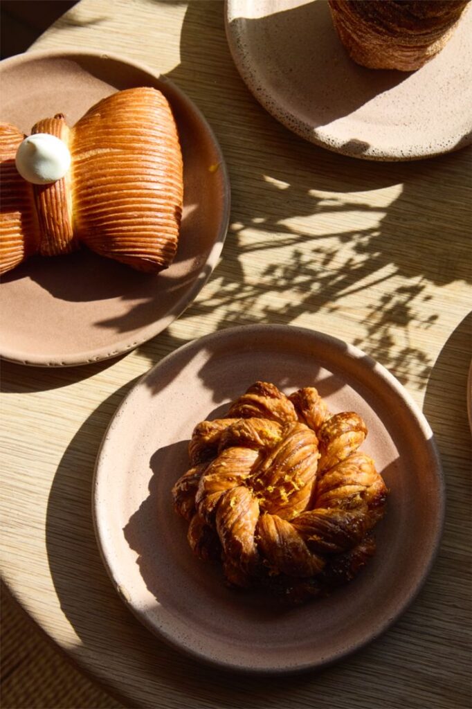 Assorted pastries on ceramic plates with natural light casting shadows on a wooden table.