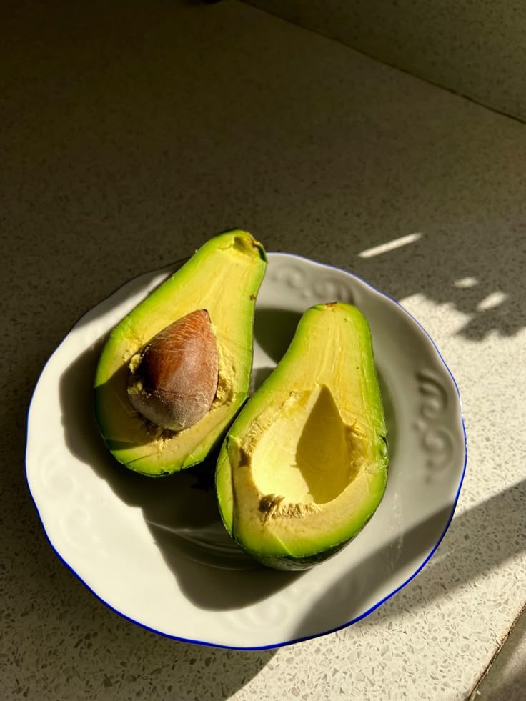 Sliced avocado on white plate in sunlight, showcasing fresh, vibrant green color and seed.