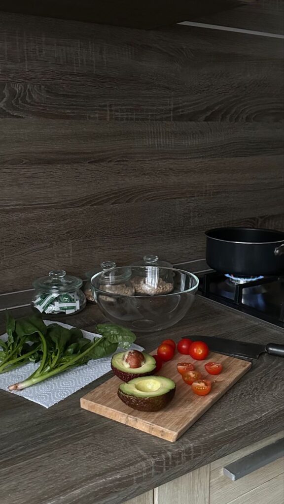 Chopping board with avocado, cherry tomatoes, and spinach on kitchen counter next to stovetop with pot.