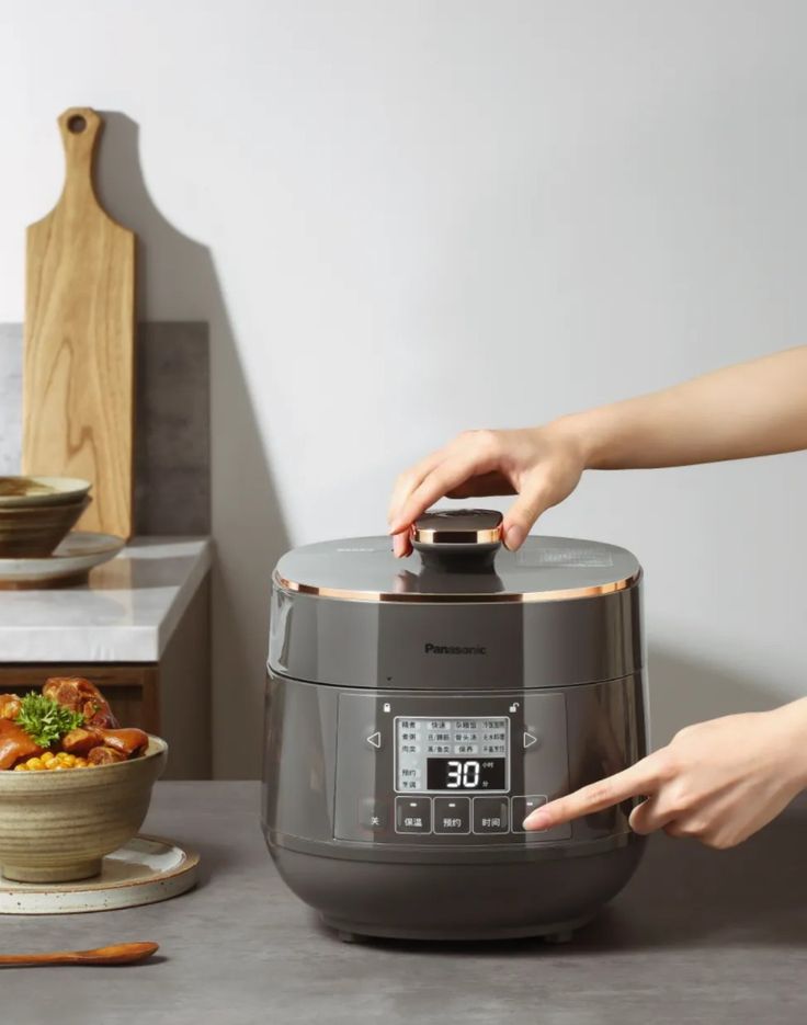 Person adjusting modern electric cooker with digital display in a kitchen setting.