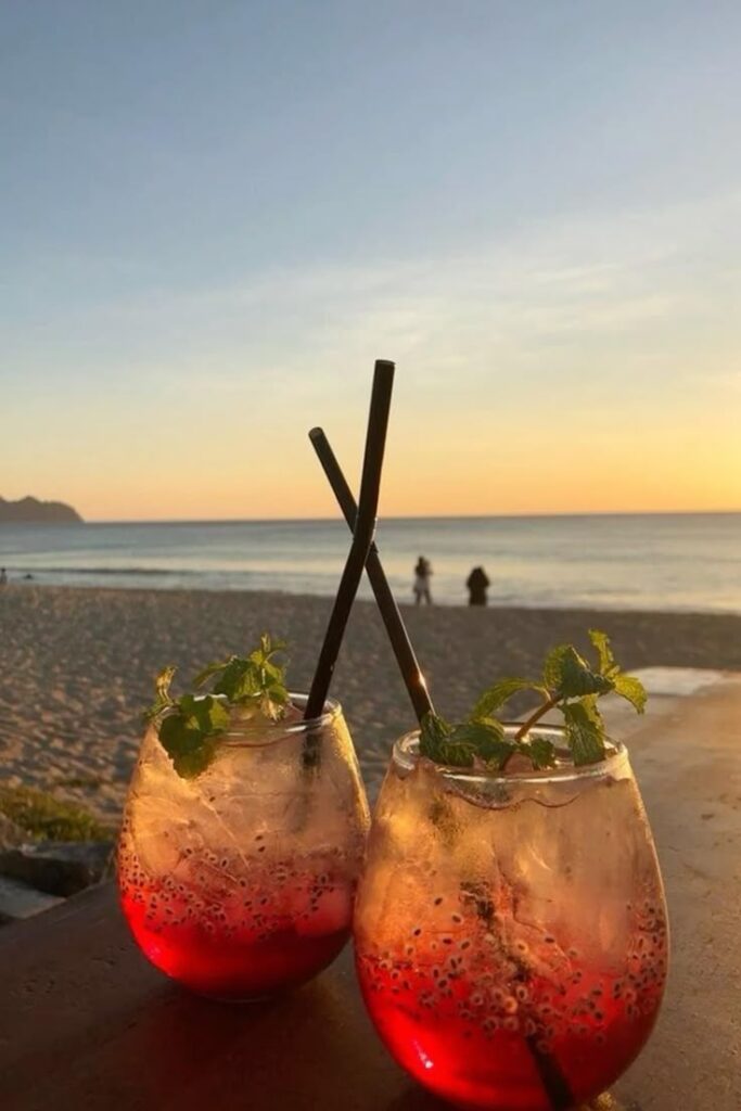 Refreshing red drinks with mint garnish on a beachside table at sunset.