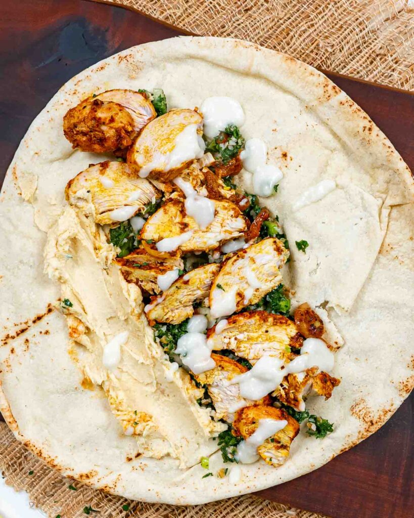 Chicken shawarma wrap with hummus, fresh greens, and creamy sauce on pita bread.