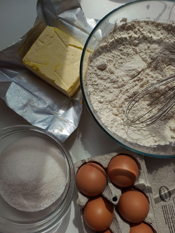 Baking ingredients: eggs, butter, flour, and sugar on a table, ready for making a cake or cookies.