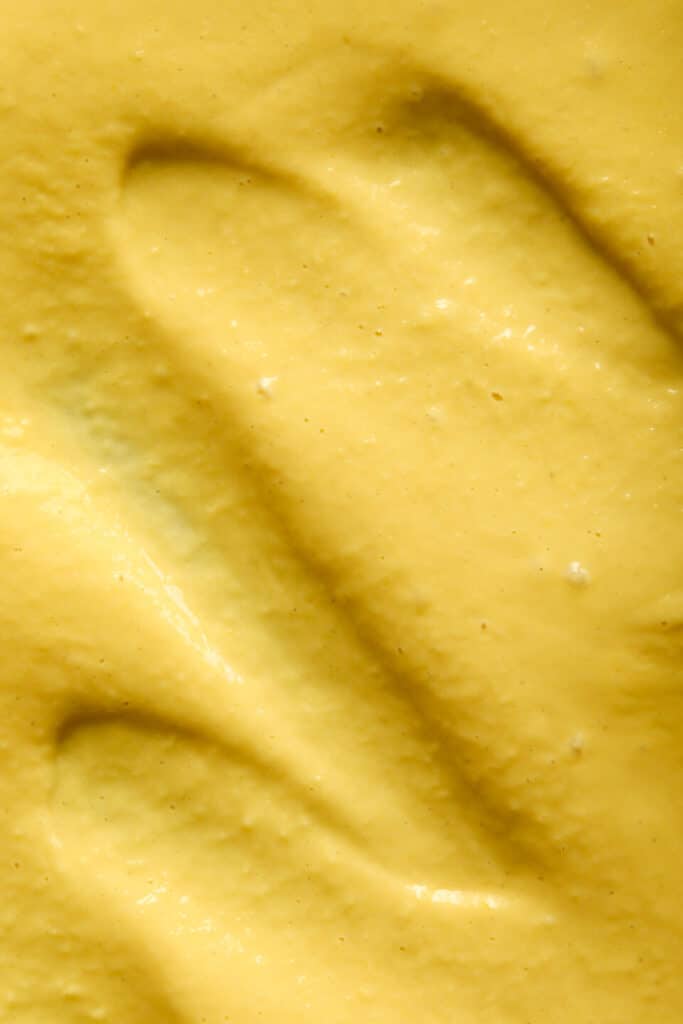 Close-up of smooth yellow mustard texture, highlighting a creamy surface with visible ridges and curves.