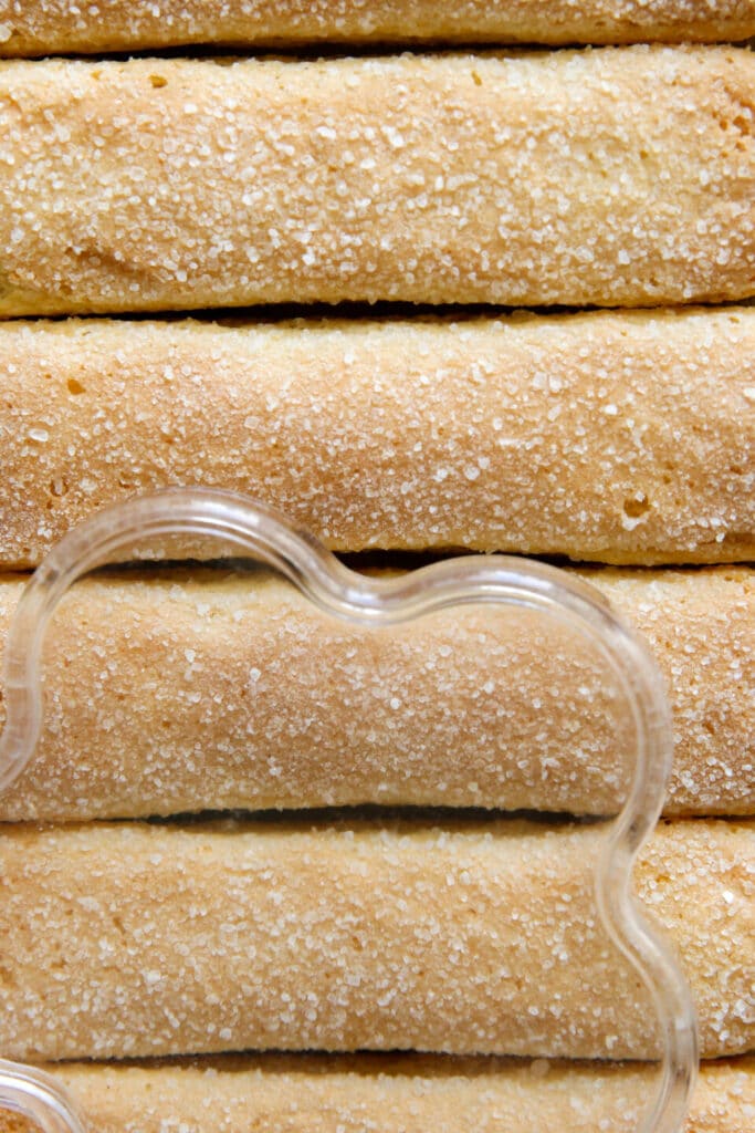 Close-up of sugar-coated ladyfinger biscuits stacked neatly with a wavy cookie cutter in the foreground.