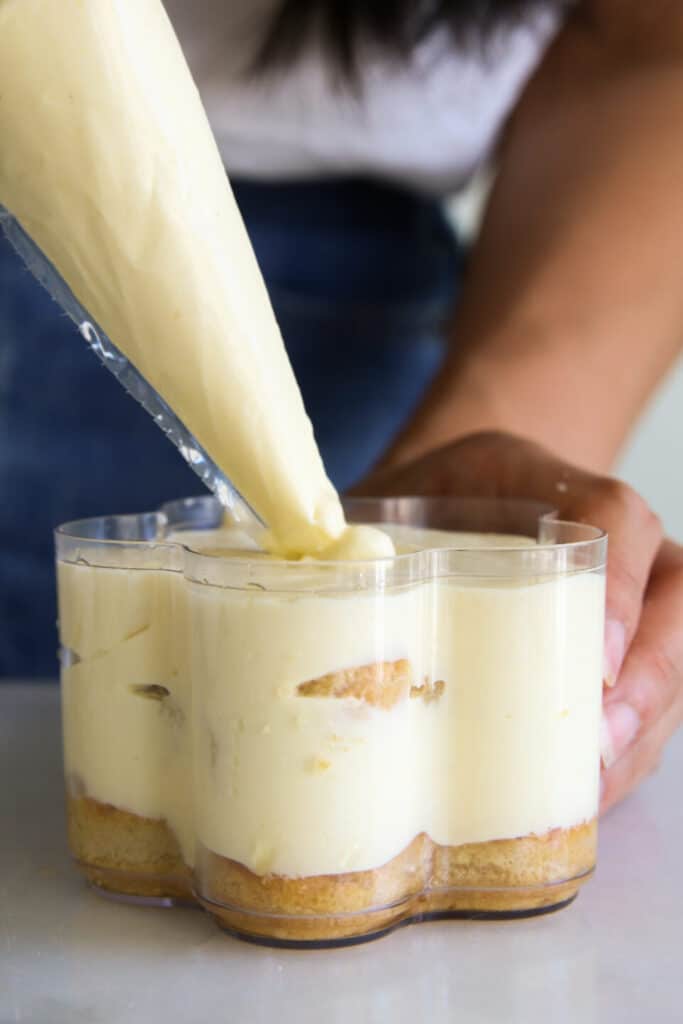 Piping creamy tiramisu layers into clear cups, showcasing a delicious homemade dessert preparation.